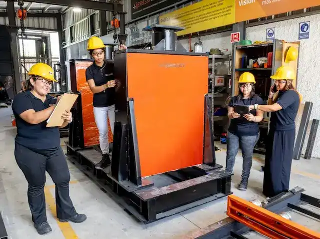Four women wearing yellow hard hats and ERBESSD INSTRUMENTS® uniforms working on the production floor around a large orange dynamic balancing machine